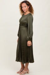 woman wearing a dark green pleated midi dress with long sleeves and a cinched waist, paired with light heels