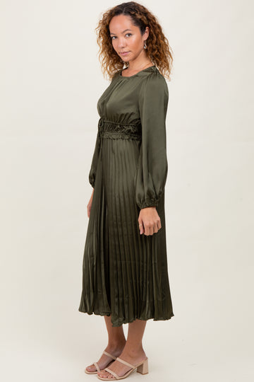 woman wearing a dark green pleated midi dress with long sleeves and a cinched waist, paired with light heels