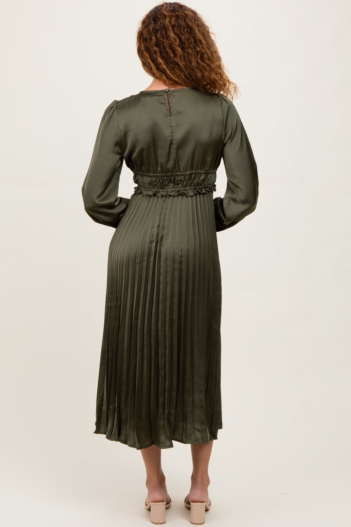 woman wearing a long olive green pleated satin dress with a fitted waist and long sleeves, shown from the back
