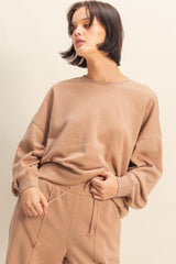 woman wearing a beige oversized sweatshirt with dropped shoulders and long sleeves, styled with matching sweatpants
