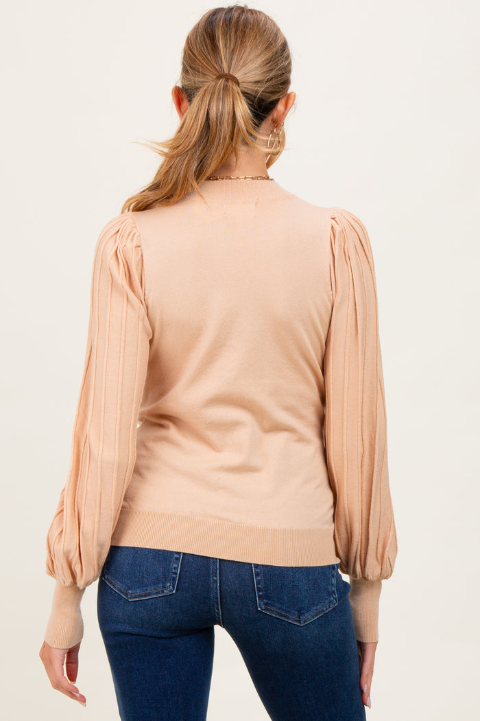 woman wearing a beige maternity sweater with puffed sleeves and ribbed cuffs, viewed from the back
