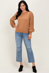 woman wearing a light brown sweater with pleated balloon sleeves and blue cropped jeans