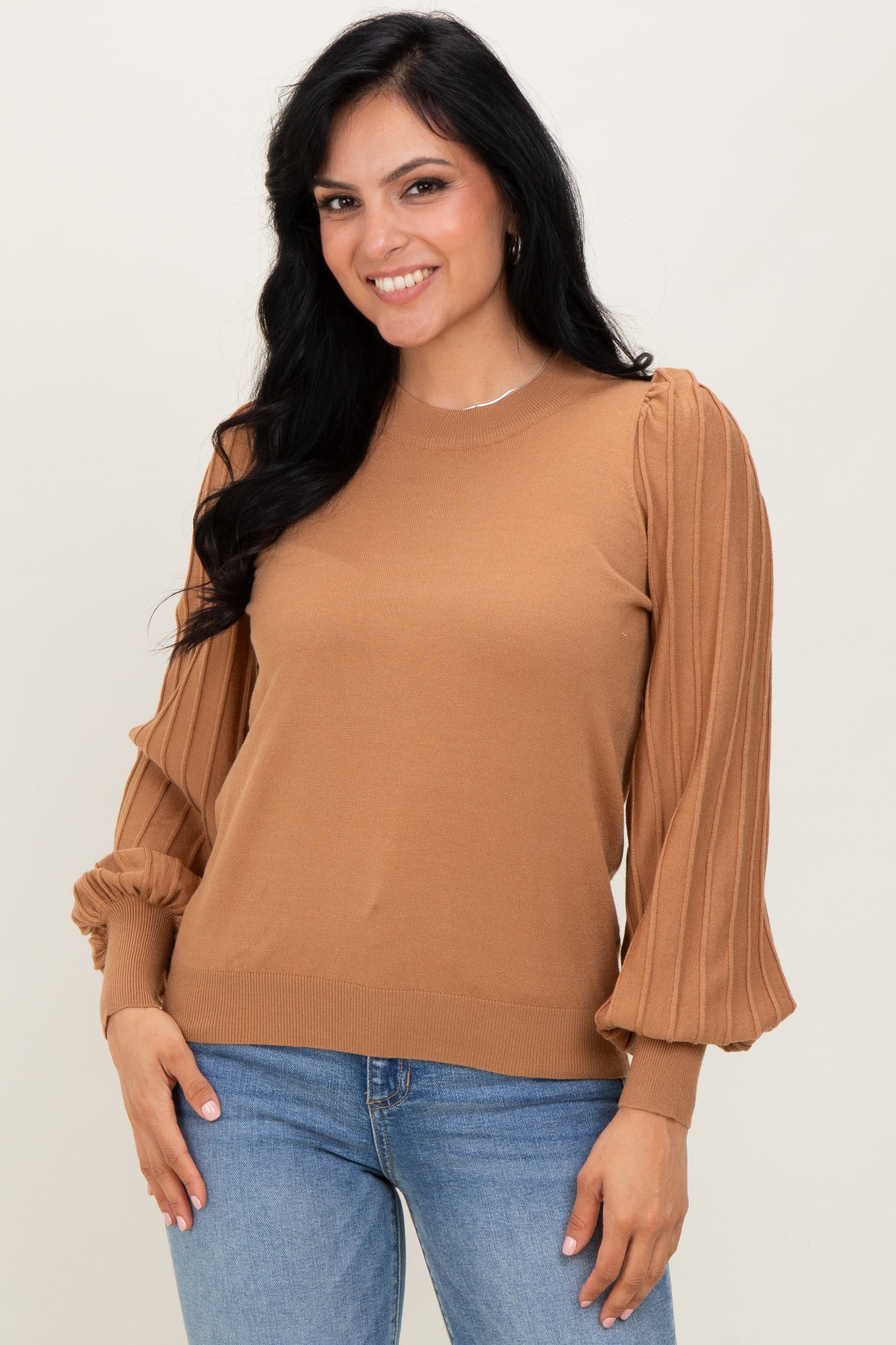woman wearing a camel ribbed sweater with puff sleeves and a fitted hem, paired with blue jeans