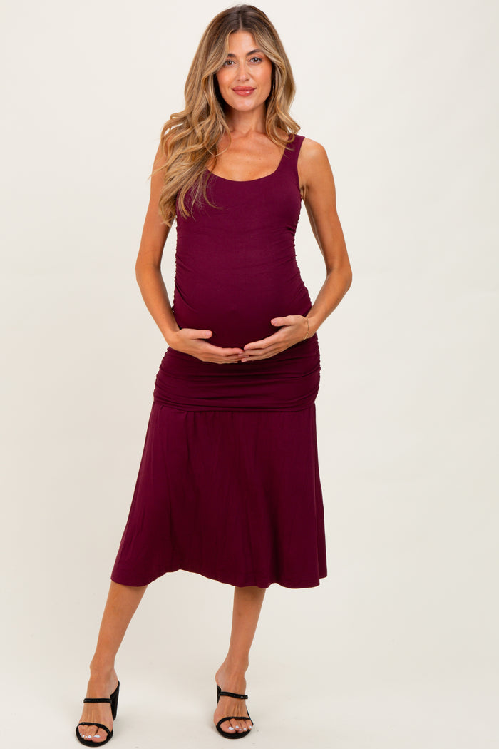 woman wearing a maroon maternity dress with a fitted bodice and flowing skirt, holding her baby bump