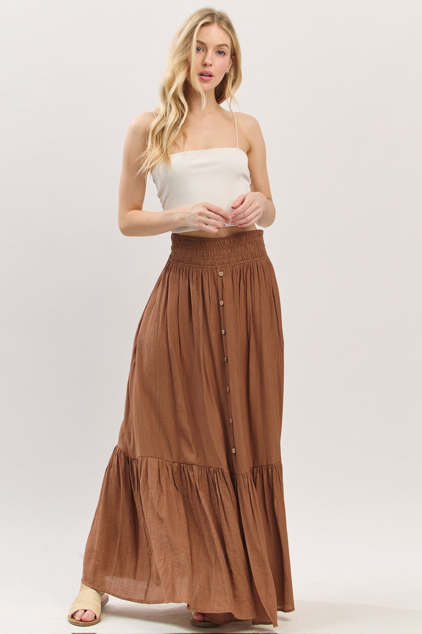 woman wearing a white spaghetti strap top and a brown maxi skirt with a tiered hem and buttons down the front