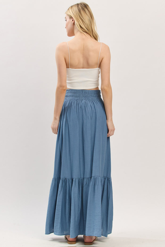 woman wearing a light blue maxi skirt with a tiered ruffle hem and elastic waistband, viewed from the back