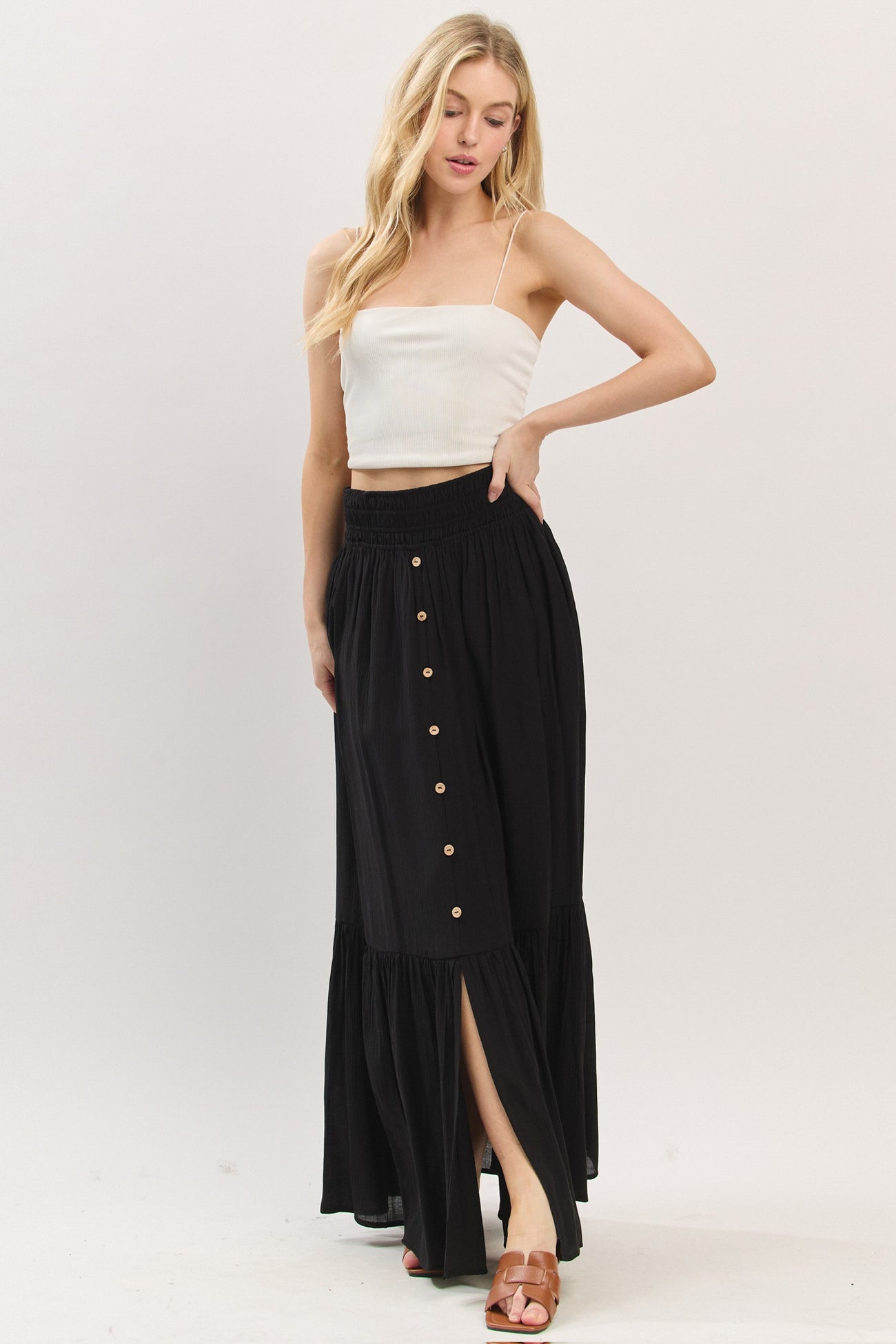 woman wearing a white cropped tank top and a black maxi skirt with buttons and a side slit