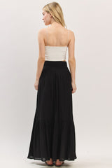 woman wearing a white spaghetti strap top and a black maxi skirt, viewed from the back
