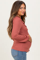 woman wearing a rust long sleeve maternity top with ruffle detailing and holding her baby bump