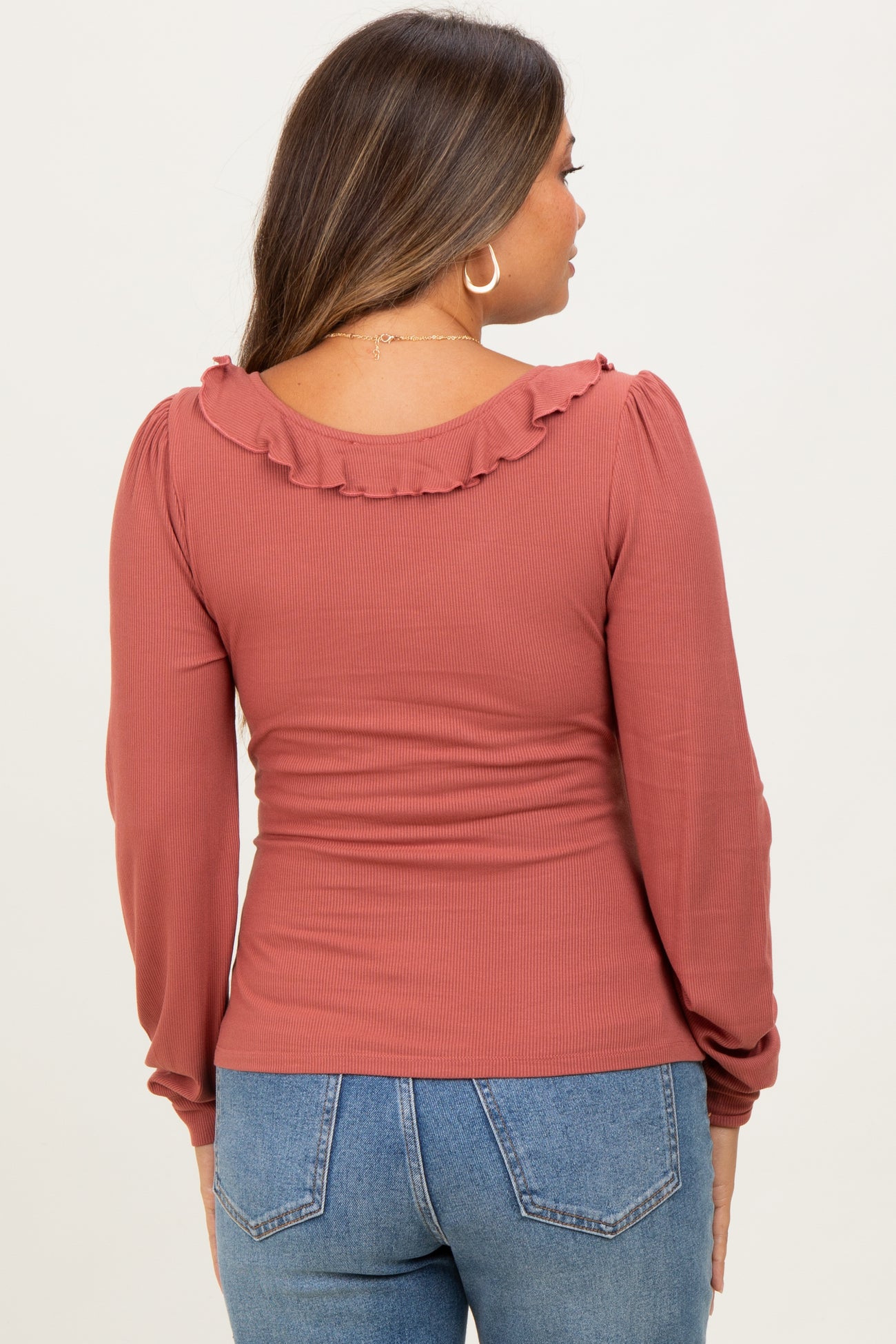 woman wearing a rust colored maternity top with ruffle detail on the neckline and long sleeves, showing a baby bump