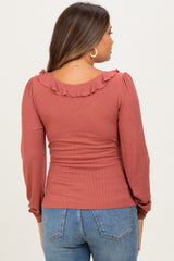 woman wearing a rust colored maternity top with ruffle detail on the neckline and long sleeves, showing a baby bump