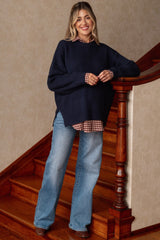 woman wearing a navy oversized knit maternity sweater over a checkered blouse and flared jeans with a visible baby bump