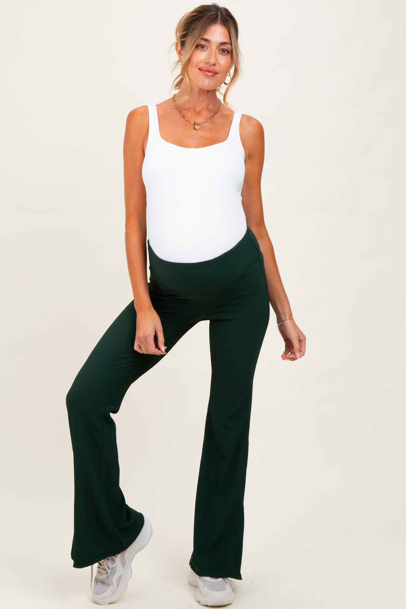 woman wearing a white maternity bodysuit and green flared maternity pants, with a visible baby bump