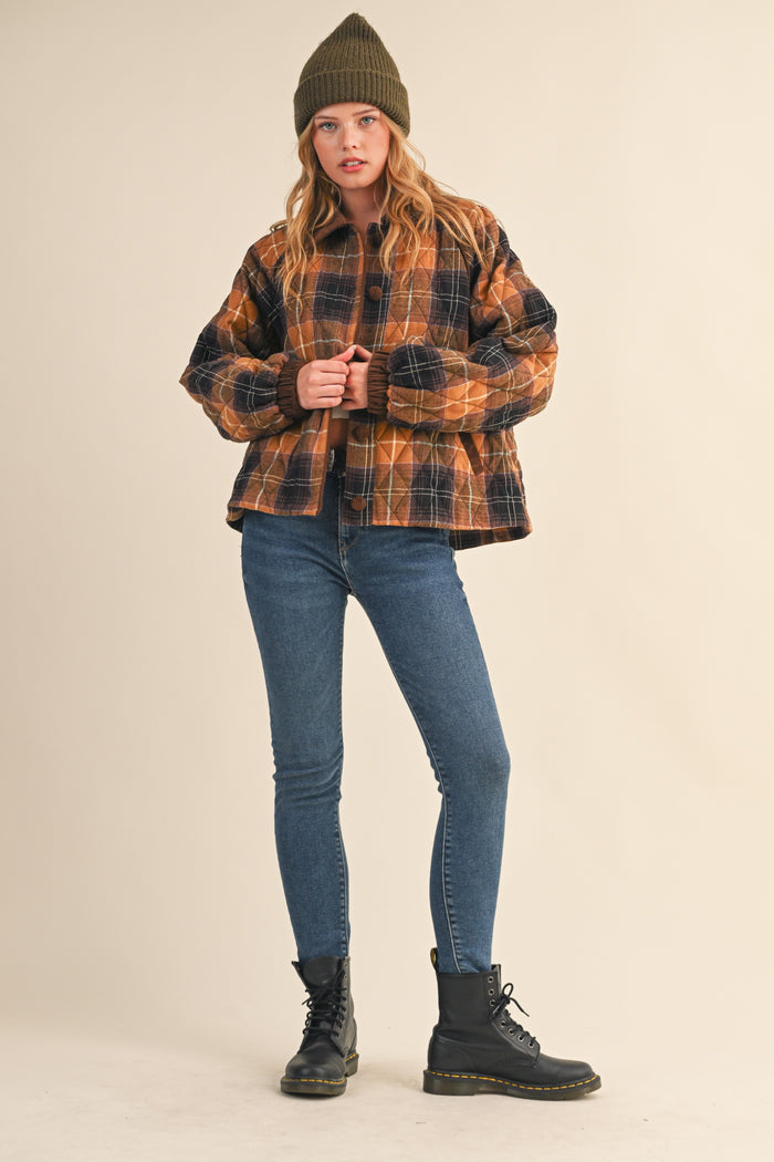 woman wearing a brown and black plaid cropped jacket with a green beanie, paired with skinny jeans and black combat boots