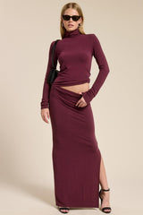 woman wearing a burgundy two-piece long sleeve top and high waist maxi skirt with a side slit and sunglasses