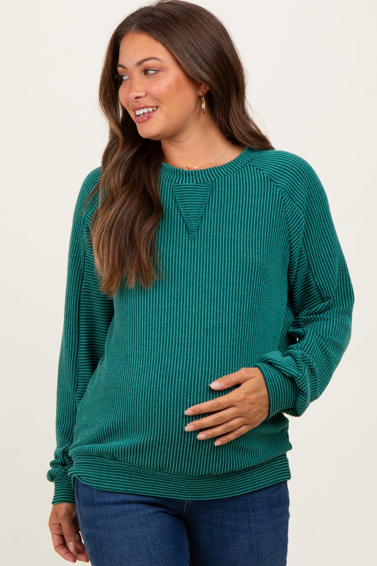 woman wearing a green ribbed maternity sweatshirt and showing her baby bump while smiling