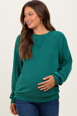 woman wearing a green ribbed maternity sweatshirt and showing her baby bump while smiling