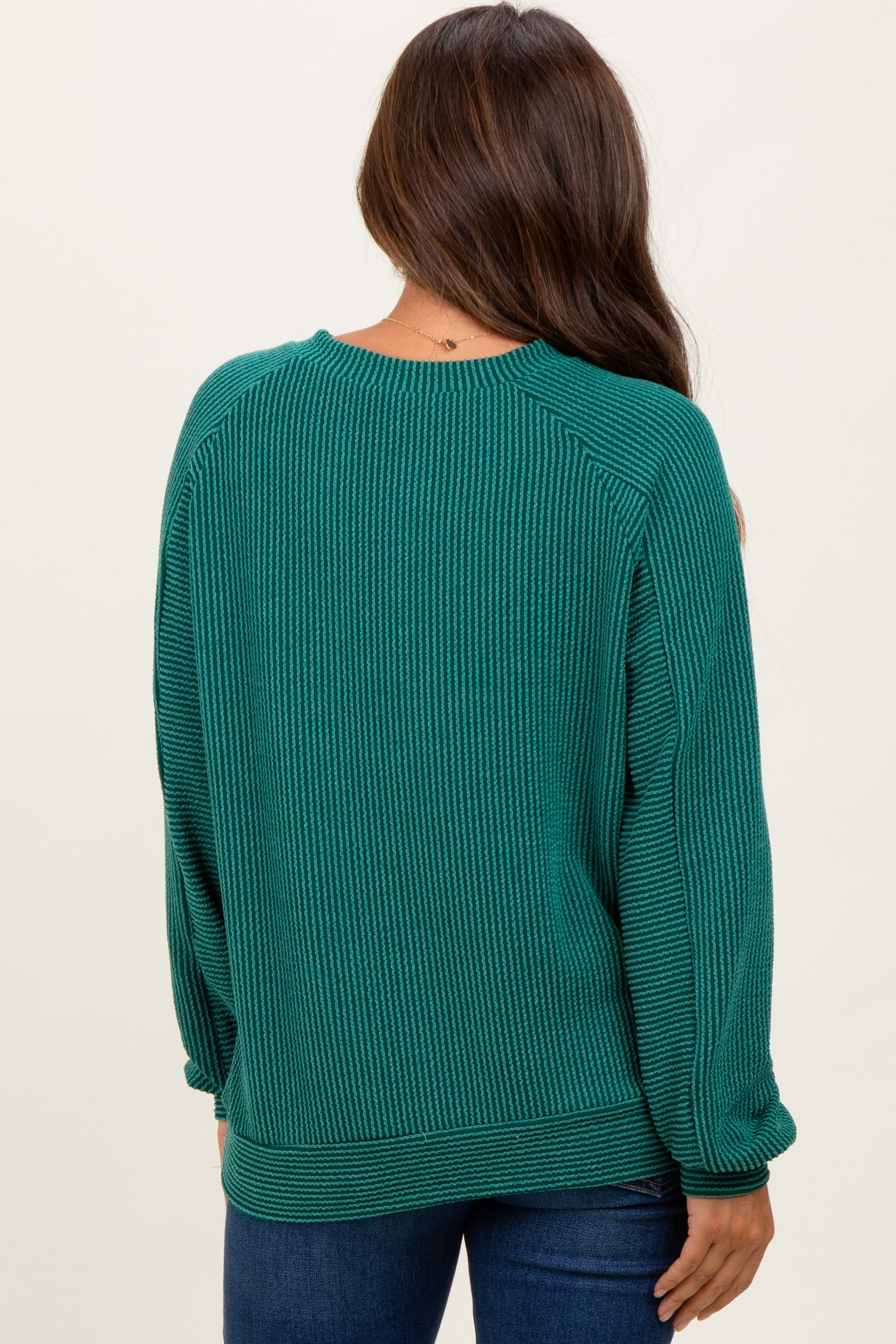woman wearing a dark green ribbed maternity sweater seen from the back, with a relaxed fit and long sleeves