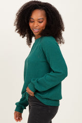 woman wearing a green ribbed knit sweater with long sleeves and a relaxed fit, smiling to the side