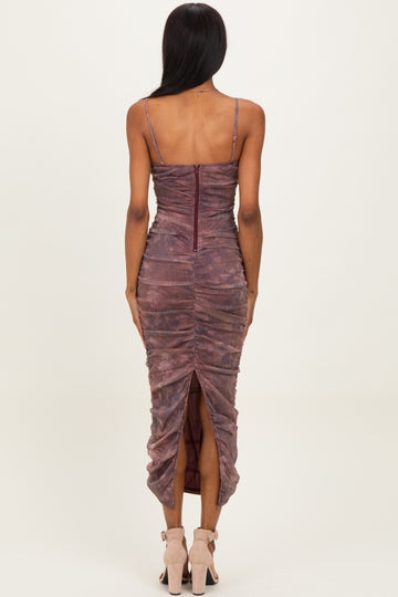 woman wearing a maroon ruched midi dress with a back zipper and a high slit