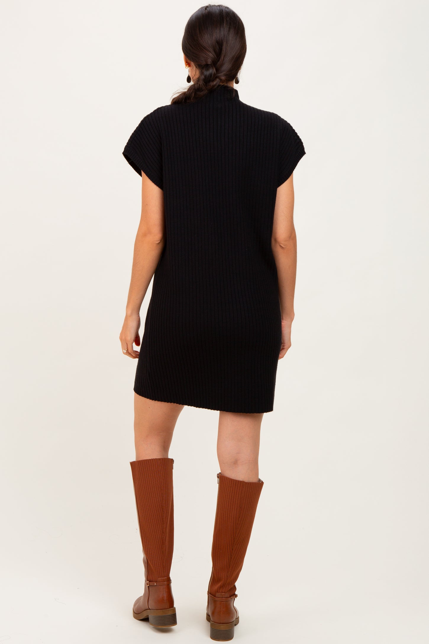 woman wearing a black ribbed short-sleeve dress and brown knee-high boots, seen from the back