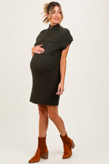 woman wearing a dark green ribbed maternity dress with short sleeves and a pocket, cradling her baby bump