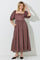 woman wearing a brown polka dot maxi dress with puff sleeves and pockets, standing against a white background