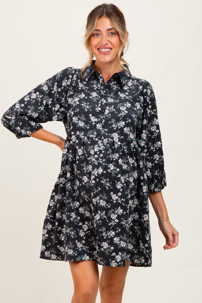 woman wearing a black floral maternity dress with a collared neckline and three-quarter sleeves, smiling and showcasing her baby bump