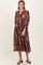 woman wearing a brown floral maxi dress with a tiered skirt and long sleeves, posing with a smile