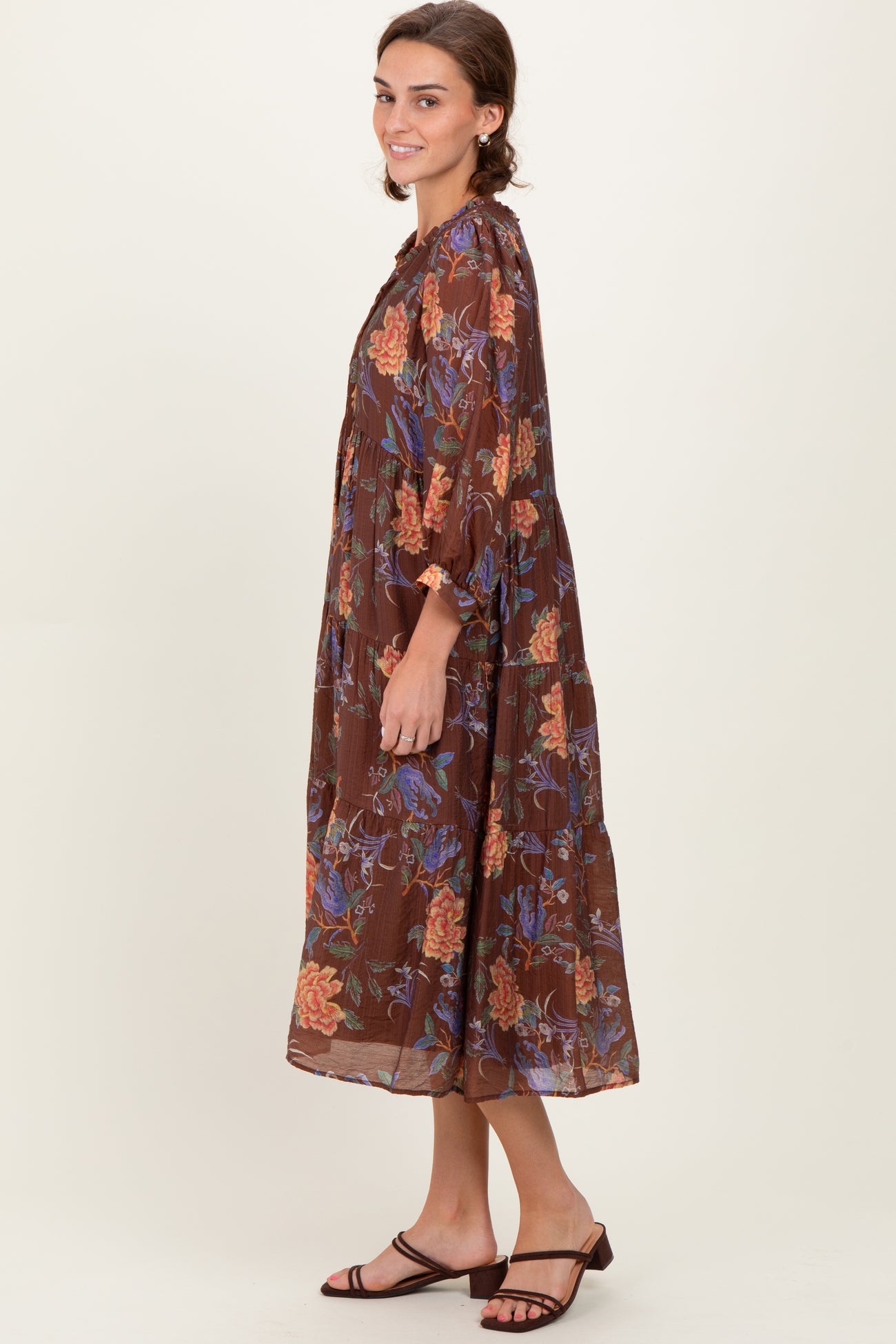 woman wearing a brown floral maxi dress with puff sleeves and tiered design paired with strappy sandals
