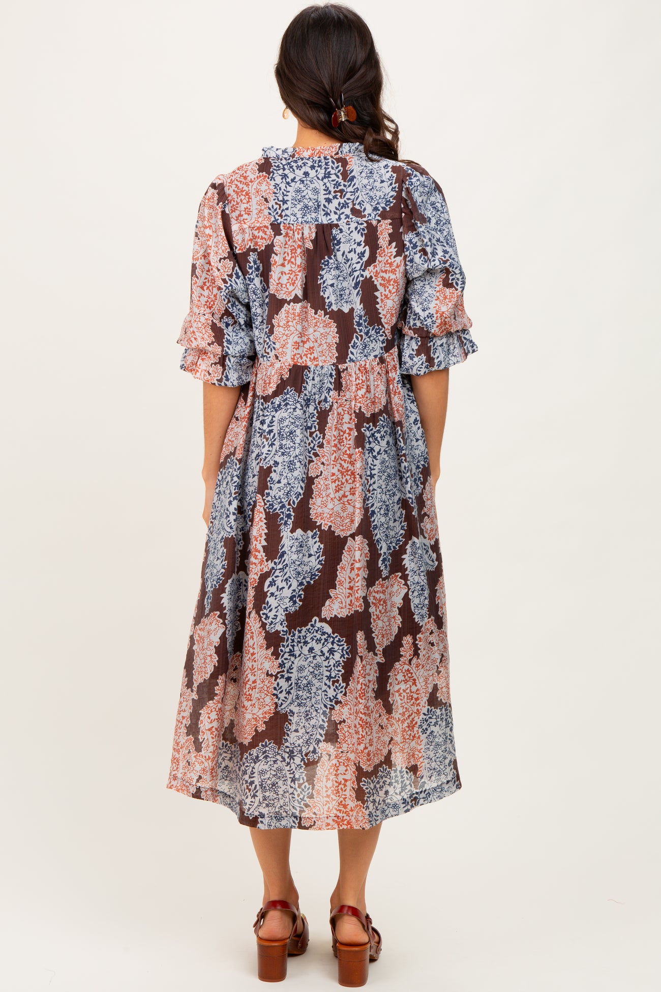 woman wearing a floral mid-length dress with ruffled sleeves and a loose fit, standing with her back to the camera