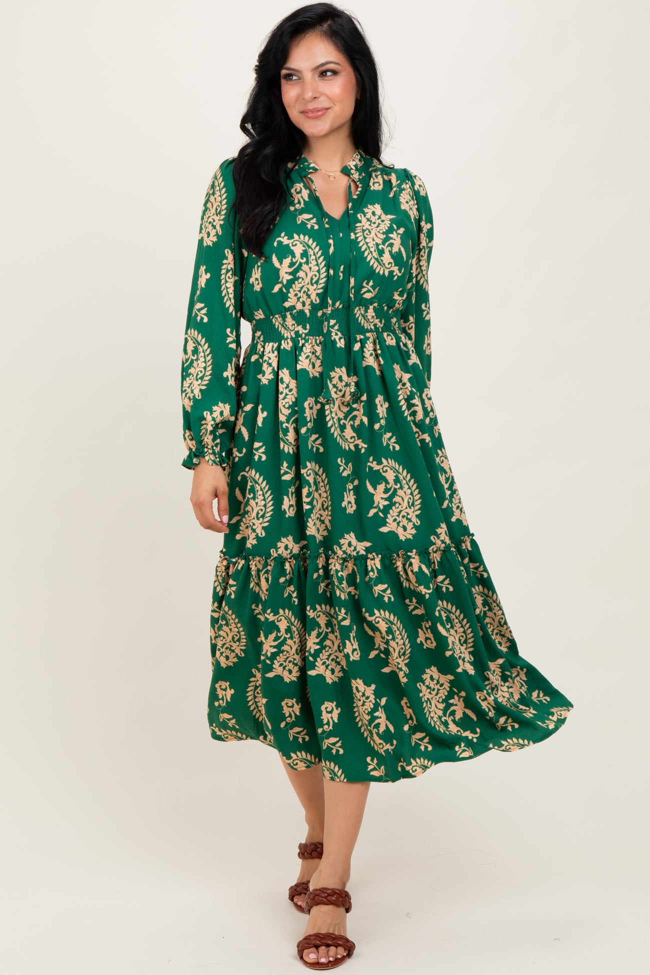 woman wearing a green floral maxi dress with long sleeves and a tiered skirt, standing on a neutral background