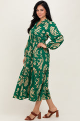 woman wearing a green floral print midi dress with long sleeves and a tiered skirt, standing profile on a light background