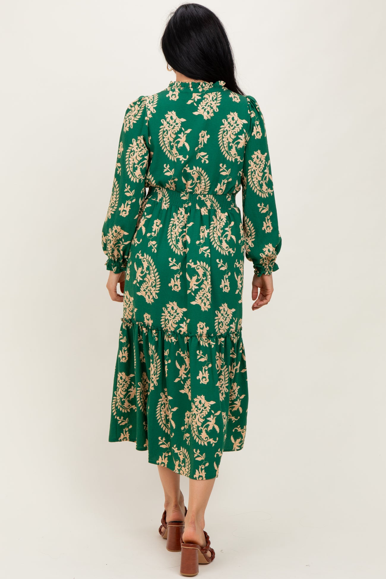 woman wearing a green floral midi dress with long sleeves and a tiered skirt, viewed from the back