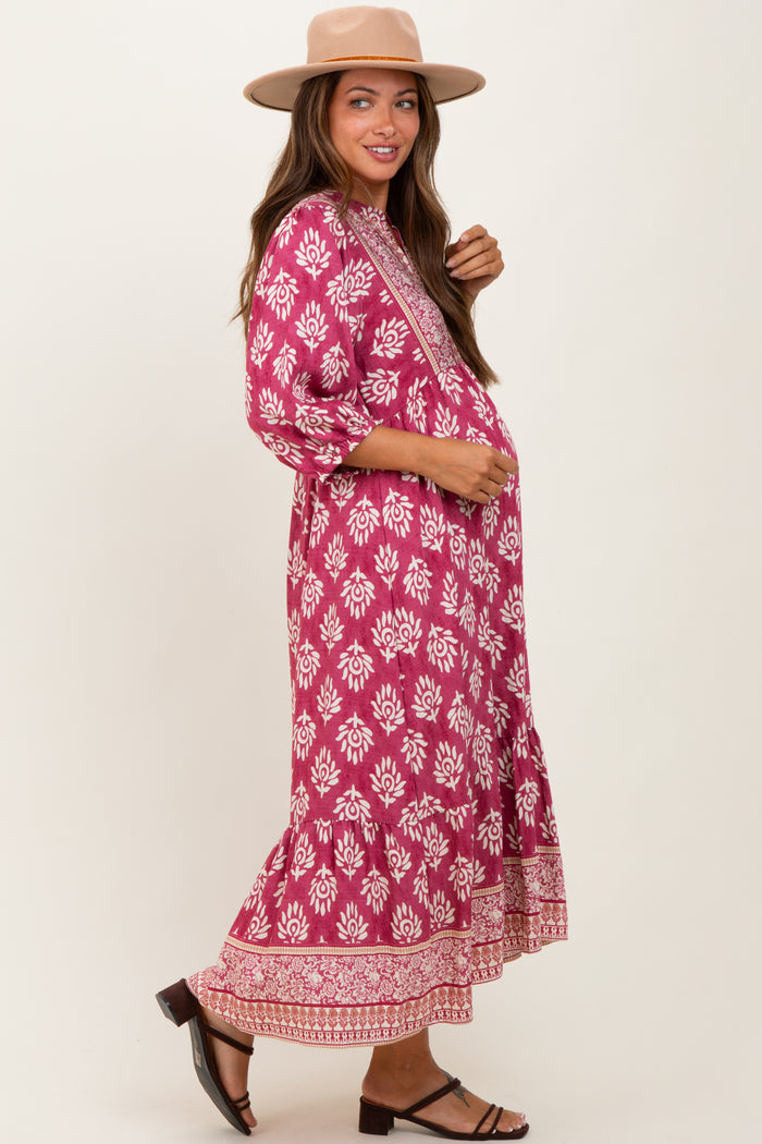 woman wearing a pink floral maternity maxi dress with three-quarter sleeves and a ruffled hem, holding her baby bump