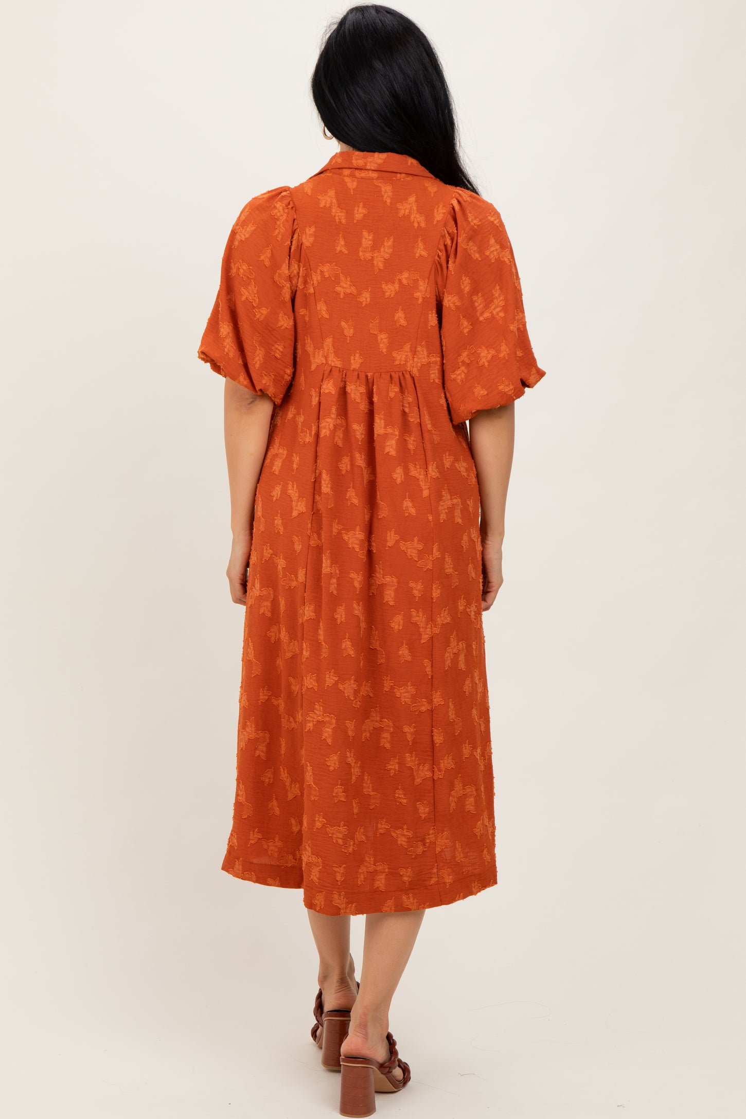 woman wearing an orange midi dress with short puff sleeves and a floral pattern, shown from the back
