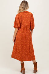 woman wearing an orange maternity dress with puffed sleeves and a flowing skirt, showing her baby bump from the back