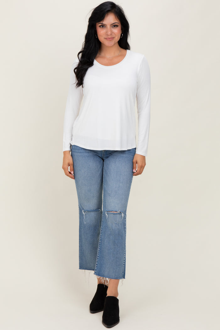 woman wearing a white long sleeve top with scoop neckline and light blue ripped jeans, standing against a neutral background