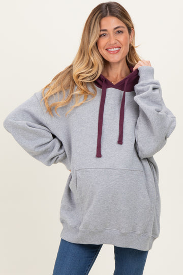 woman wearing a gray maternity hoodie with a maroon hood and pockets styled with blue jeans