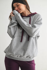 woman wearing a gray oversized hoodie with burgundy drawstrings and matching joggers, smiling and posing against a plain background