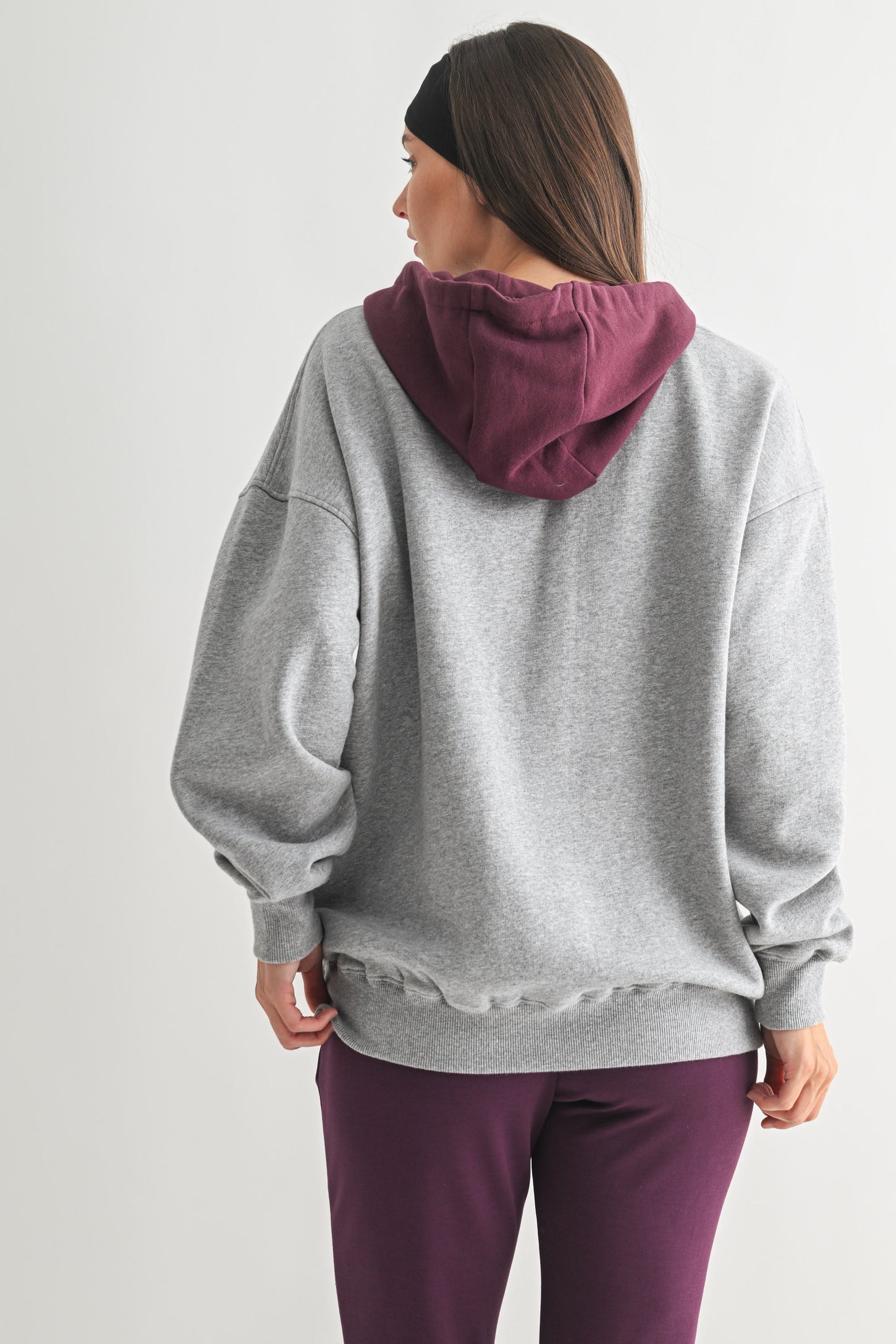 woman wearing a gray oversized hoodie with a maroon hood and matching purple sweatpants, viewed from the back