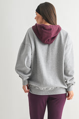 woman wearing a gray oversized hoodie with a maroon hood and matching purple sweatpants, viewed from the back