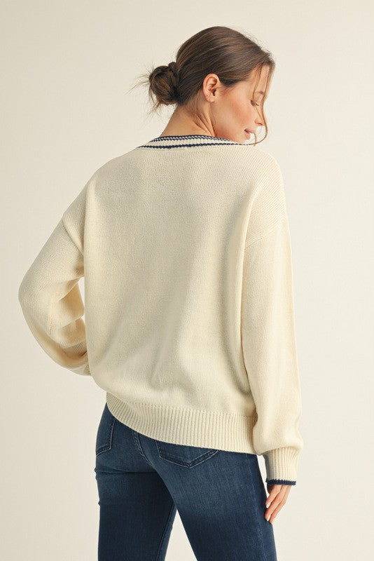 woman wearing a cream oversized sweater with navy stripe detail on the neckline, turned slightly to show the back