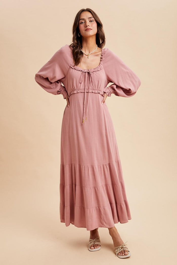 woman wearing a dusty pink long sleeve maxi dress with a tiered skirt and drawstring detail around the neckline
