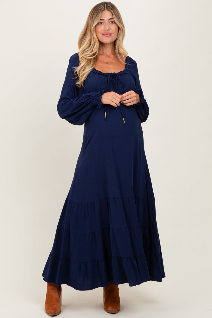 woman wearing a navy blue long sleeve maternity maxi dress with tiered ruffles and adjustable drawstring neckline, showing baby bump