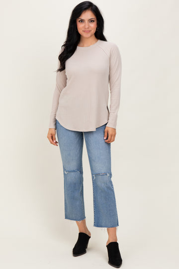 woman wearing a beige long sleeve ribbed top with a curved hem and light blue frayed hem jeans