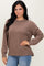 woman wearing a brown ribbed long sleeve sweater paired with blue jeans, posing with a smile