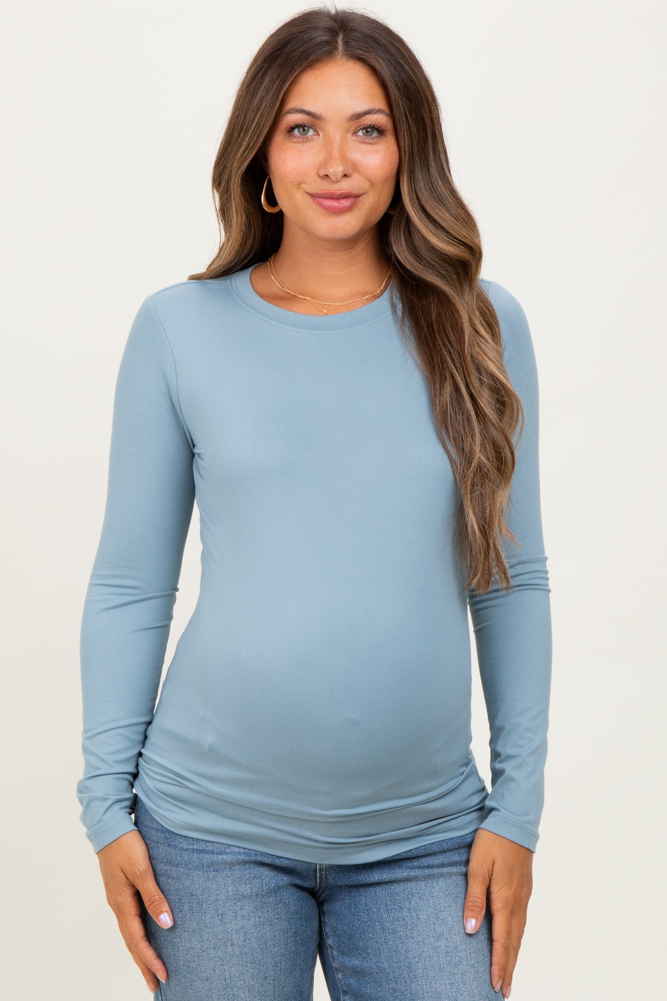 woman wearing a light blue long sleeve maternity top and showing her baby bump