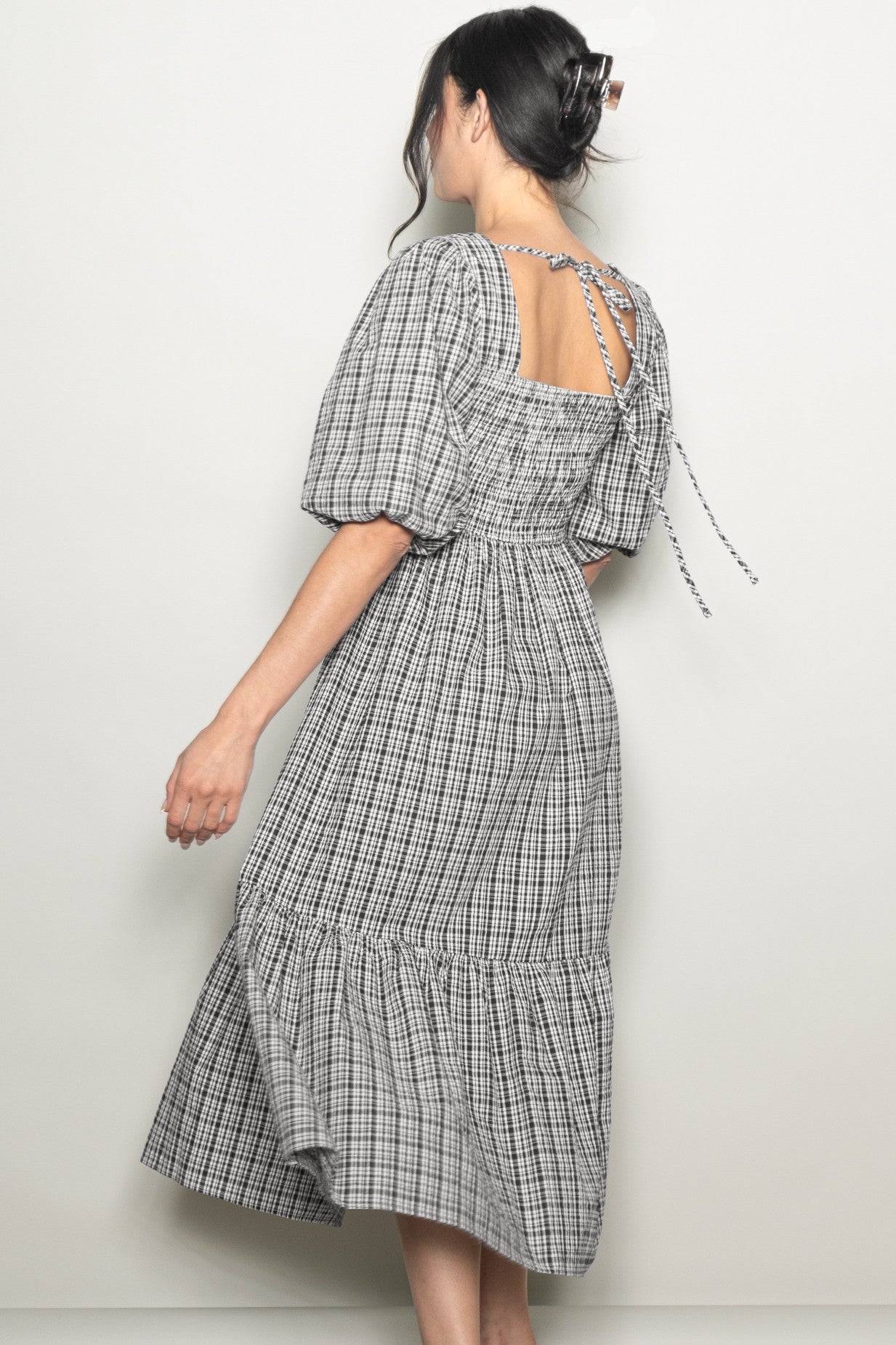 woman wearing a black and white gingham midi dress with puff sleeves and a tied open back detail