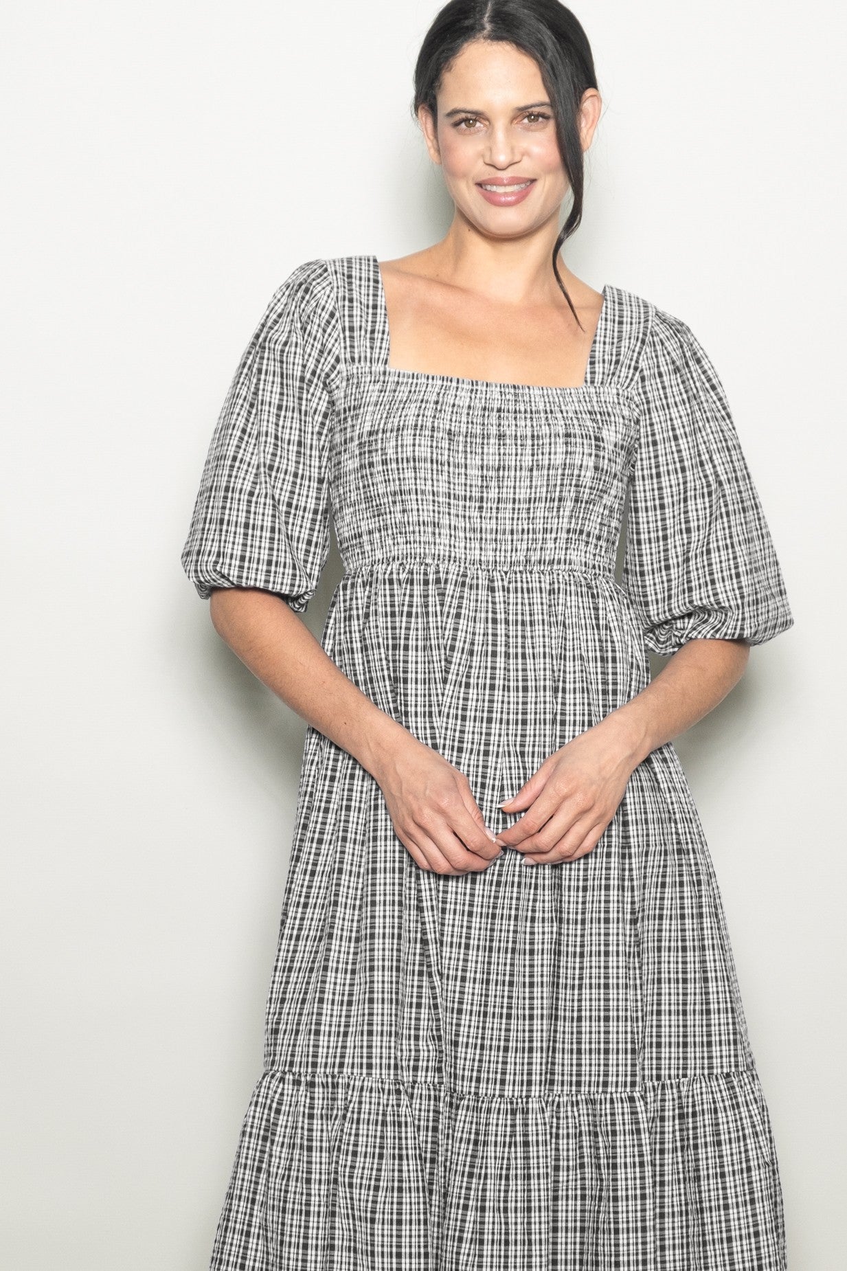 woman wearing a black and white checkered puff sleeve dress with a square neckline and tiered skirt